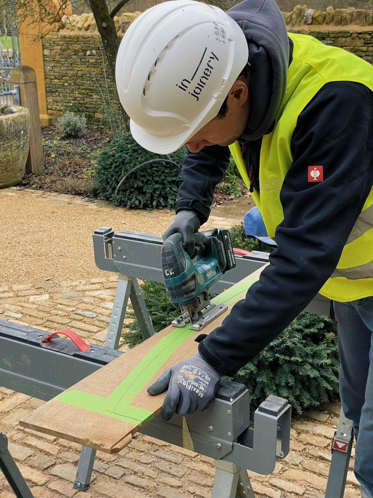 Man in hardhat cutting wood with a jigsaw.